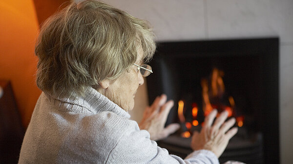 An elderly lady warming herself up with a fire.