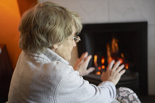 An elderly lady warming herself up with a fire.